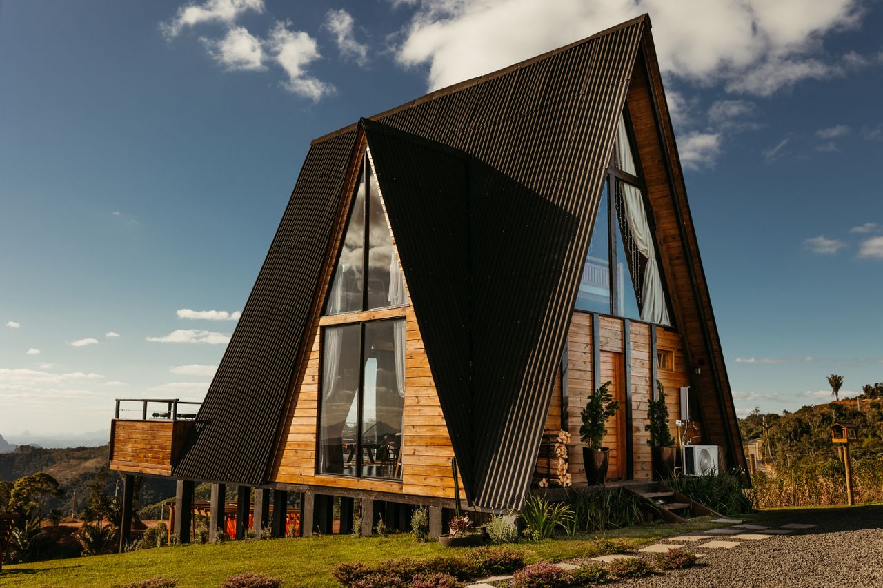 A picturesque A-frame wooden cabin on stilts amidst lush greenery in Brazil's rural landscape.